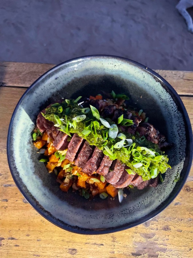 Sliced steak with fresh herbs in a dark ceramic bowl